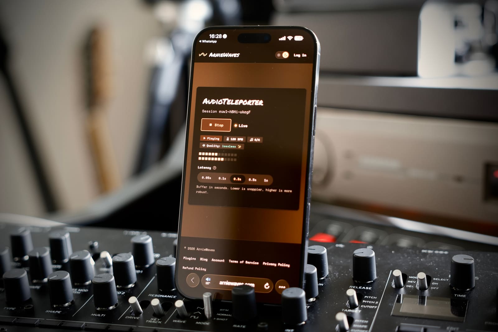 The AudioTeleporter listen player open in a phone browser, propped on a synth in a studio